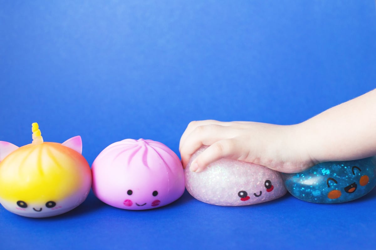A child's hand squeezing a bright, soft squishy toy